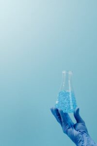 Blue-gloved hand holding a flask filled with a blue substance in a lab.