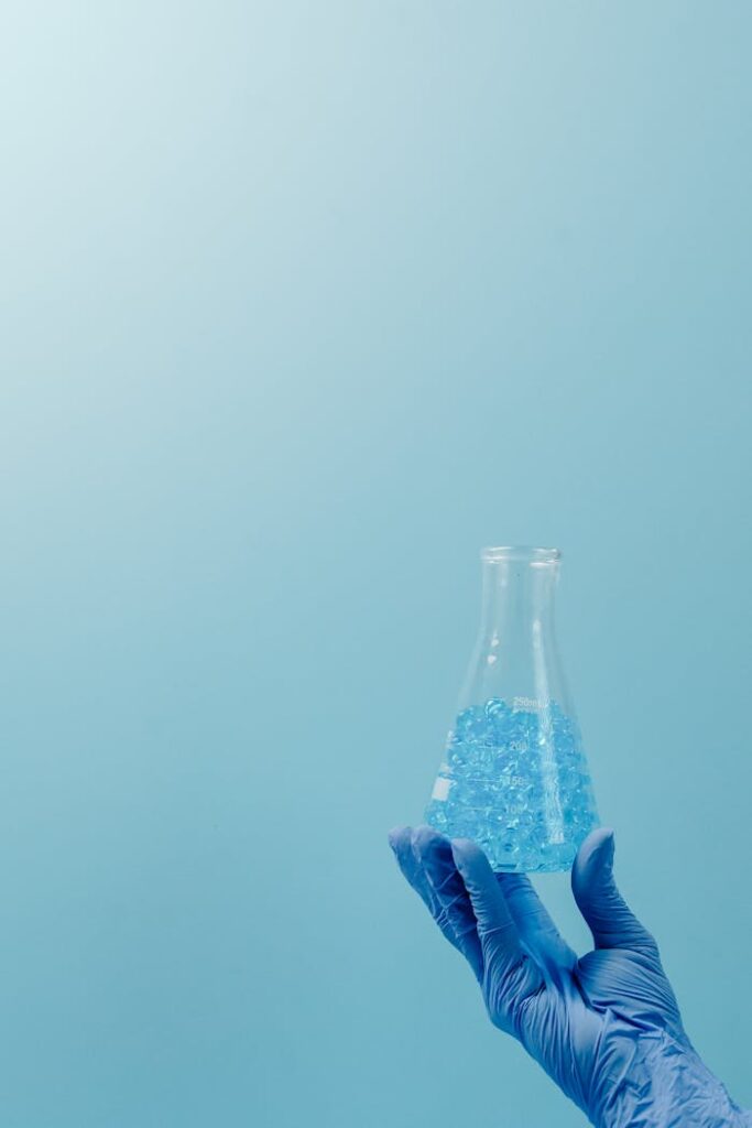 Blue-gloved hand holding a flask filled with a blue substance in a lab.